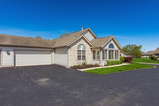 ranch-style house with a garage, a front lawn, stone siding, a shingled roof, and driveway