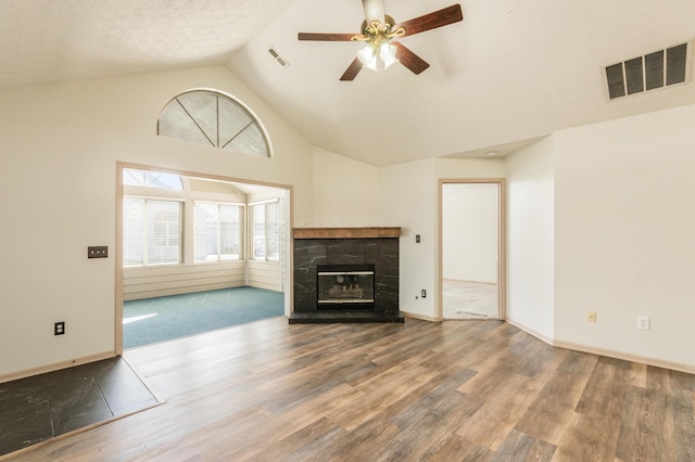 unfurnished living room with a stone fireplace, a ceiling fan, wood finished floors, and visible vents