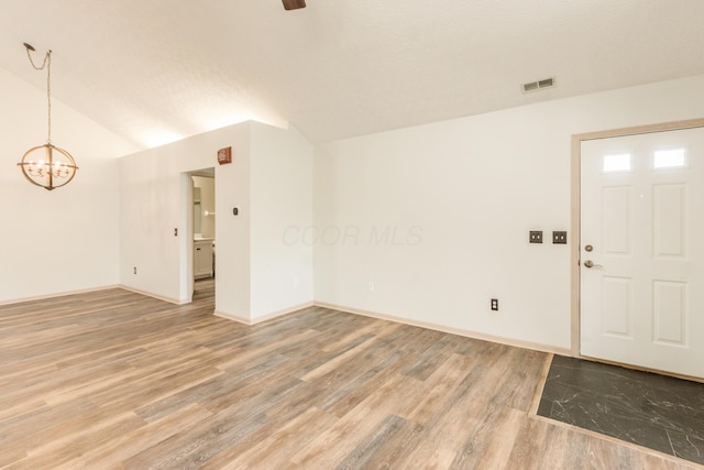 spare room with visible vents, an inviting chandelier, lofted ceiling, light wood-style floors, and baseboards