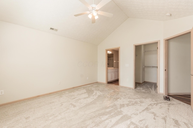 unfurnished bedroom featuring visible vents, light colored carpet, a spacious closet, ensuite bath, and vaulted ceiling