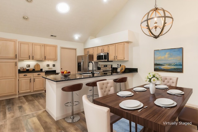 kitchen featuring light brown cabinetry, dark countertops, a sink, stainless steel appliances, and a peninsula