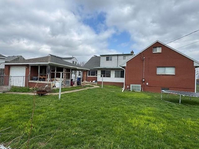 back of house featuring a trampoline, a yard, central AC, and brick siding