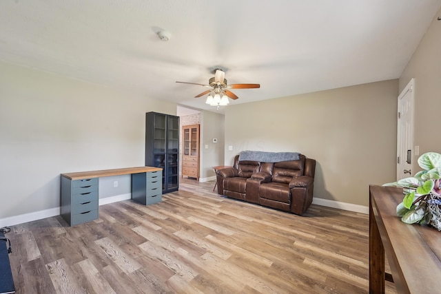 living room featuring baseboards, light wood-style flooring, and ceiling fan