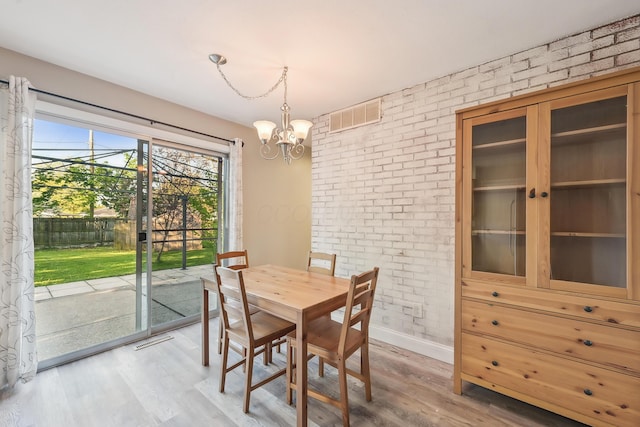 dining space featuring brick wall, visible vents, light wood-type flooring, baseboards, and a chandelier