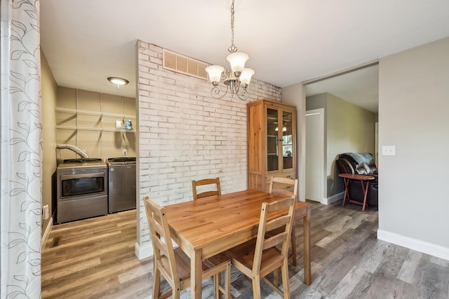 dining room with brick wall, visible vents, wood finished floors, a chandelier, and washer and clothes dryer
