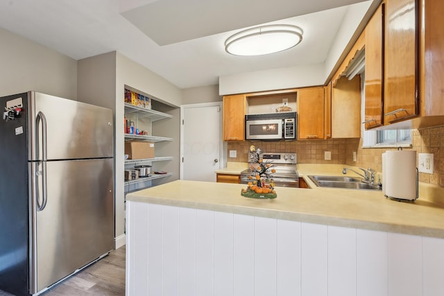 kitchen with a peninsula, open shelves, appliances with stainless steel finishes, and a sink
