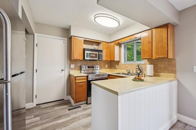 kitchen featuring brown cabinets, light wood-style floors, light countertops, stainless steel appliances, and a peninsula
