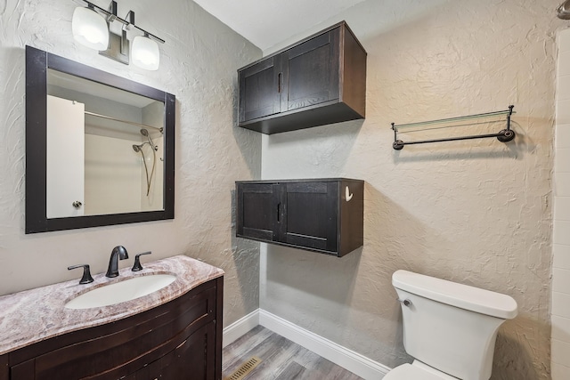 bathroom featuring a textured wall, vanity, toilet, baseboards, and wood finished floors