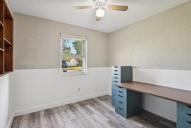 unfurnished office with a textured wall, ceiling fan, wood finished floors, and wainscoting