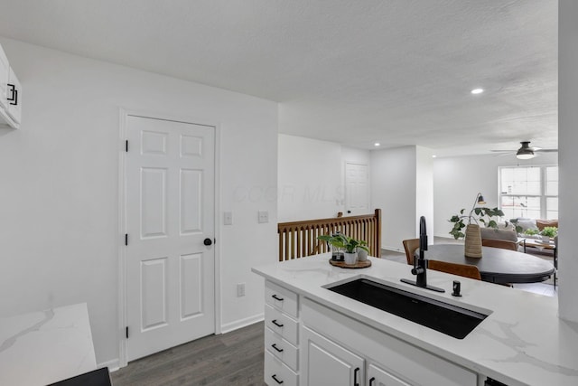 kitchen featuring light stone counters, white cabinets, a sink, ceiling fan, and dark wood finished floors