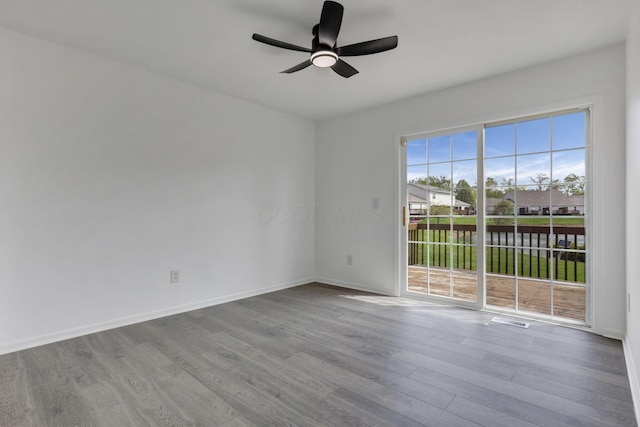 spare room with wood finished floors, a ceiling fan, visible vents, and baseboards