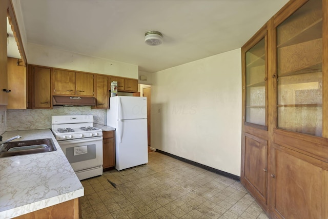 kitchen featuring white appliances, brown cabinets, under cabinet range hood, and a sink