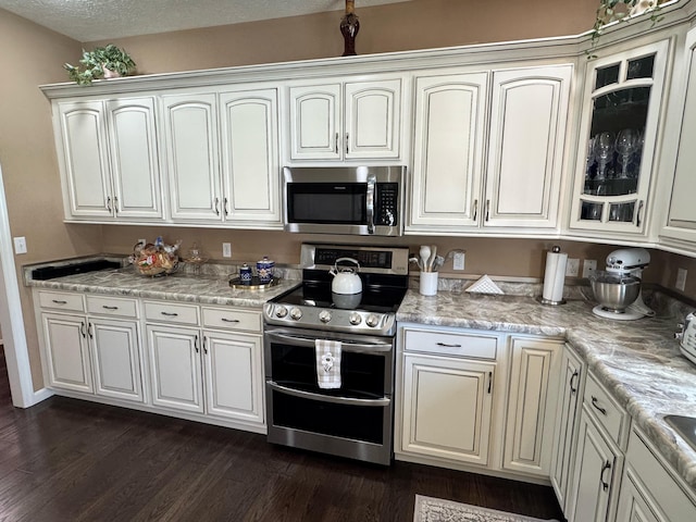 kitchen featuring glass insert cabinets, dark wood-style flooring, stainless steel appliances, and light countertops