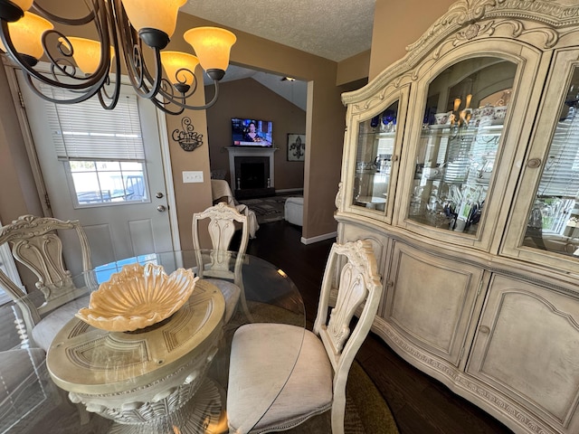 dining space featuring dark wood finished floors, an inviting chandelier, a textured ceiling, and vaulted ceiling
