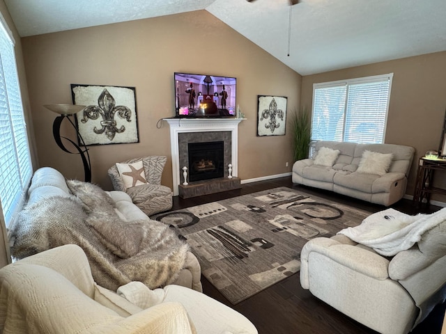 living room with a tiled fireplace, a ceiling fan, vaulted ceiling, baseboards, and wood finished floors