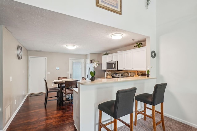 kitchen with a kitchen breakfast bar, tasteful backsplash, baseboards, white cabinets, and appliances with stainless steel finishes