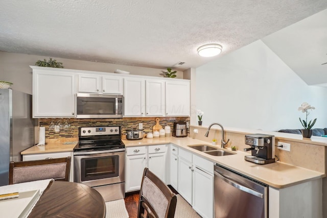 kitchen with stainless steel appliances, a peninsula, light countertops, and a sink