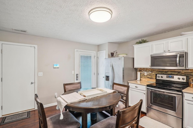 kitchen with white cabinets, appliances with stainless steel finishes, light countertops, dark wood finished floors, and backsplash