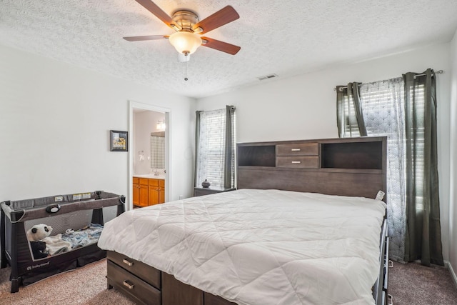 carpeted bedroom featuring ceiling fan, ensuite bathroom, a sink, visible vents, and a textured ceiling