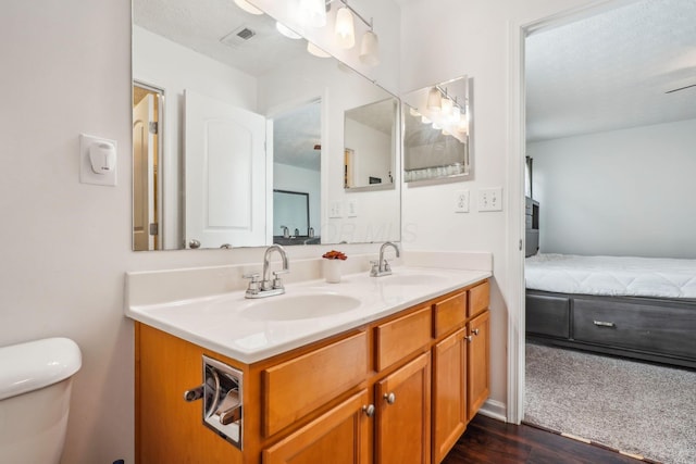 full bath with toilet, double vanity, a sink, and wood finished floors