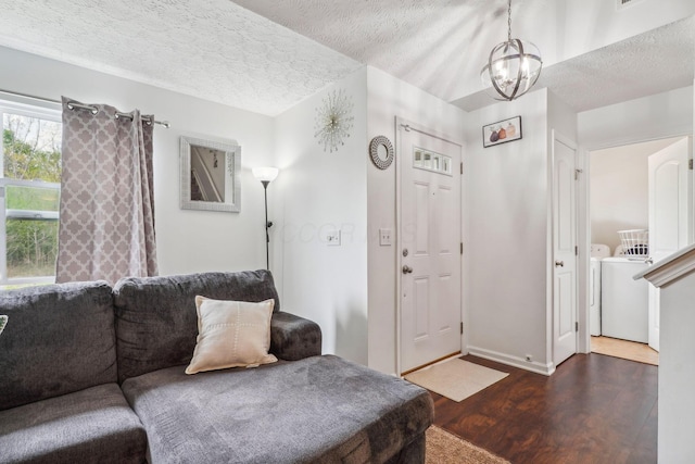living room featuring a textured ceiling, washing machine and clothes dryer, a chandelier, baseboards, and wood finished floors