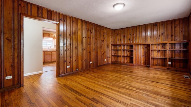 empty room with wood finished floors, a textured ceiling, a sink, visible vents, and wooden walls