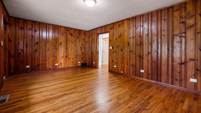 unfurnished room with wood walls, a textured ceiling, visible vents, and wood-type flooring