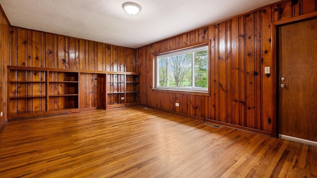 spare room with hardwood / wood-style floors, visible vents, wooden walls, and baseboards
