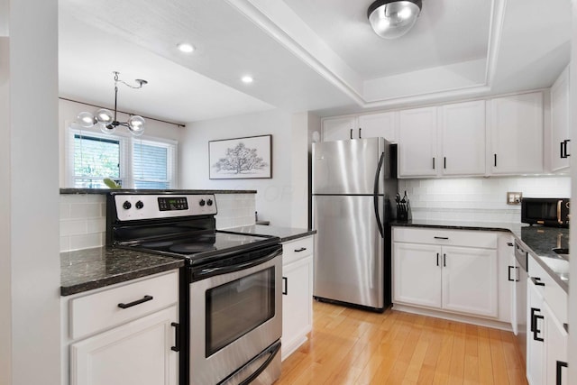 kitchen with light wood-type flooring, dark stone counters, white cabinets, appliances with stainless steel finishes, and backsplash