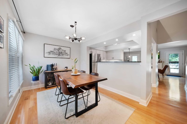 dining room with baseboards, a raised ceiling, an inviting chandelier, recessed lighting, and light wood-style flooring