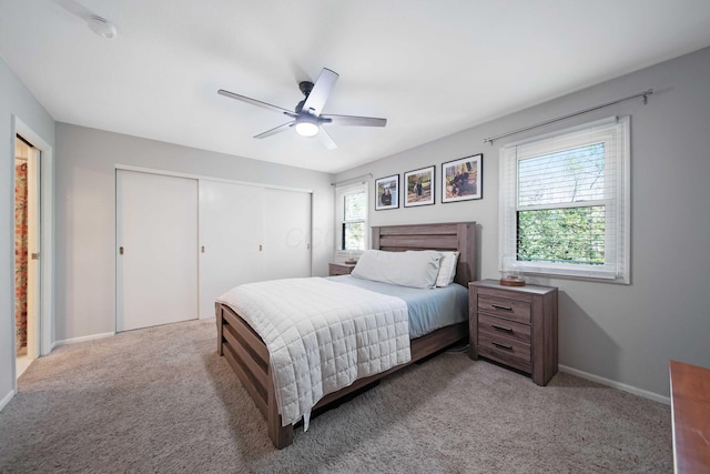 bedroom with a closet, baseboards, ceiling fan, and light carpet