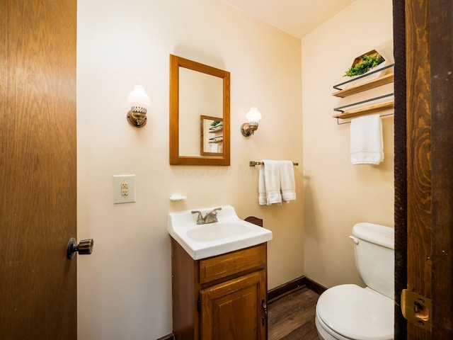 half bath featuring toilet, baseboards, wood finished floors, and vanity