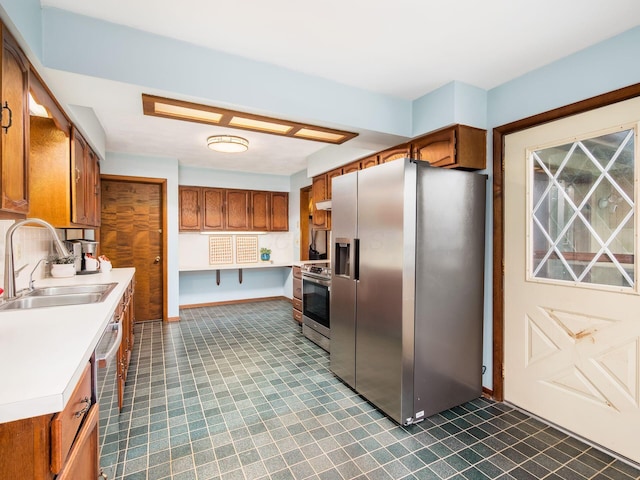 kitchen with brown cabinetry, appliances with stainless steel finishes, a sink, baseboards, and light countertops