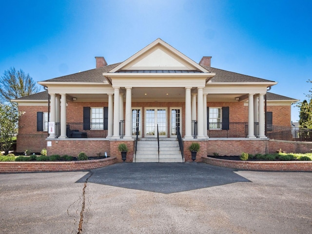 neoclassical home with covered porch, brick siding, and a chimney