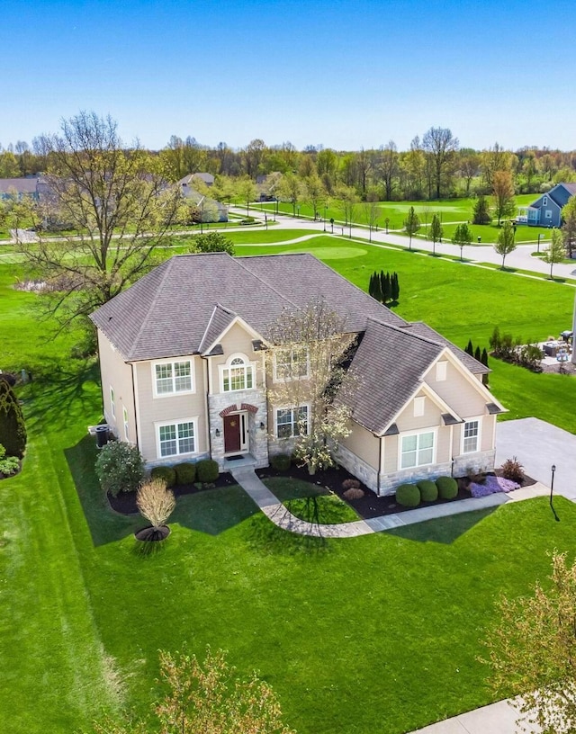 view of front of home featuring a shingled roof, a front lawn, and stone siding
