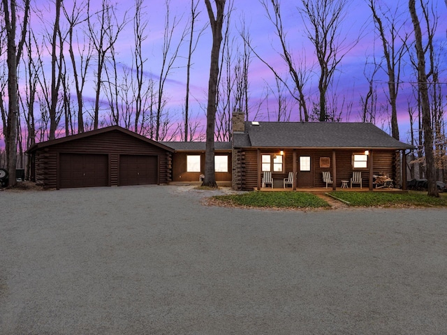 view of front of house with covered porch, a chimney, log siding, a garage, and gravel driveway