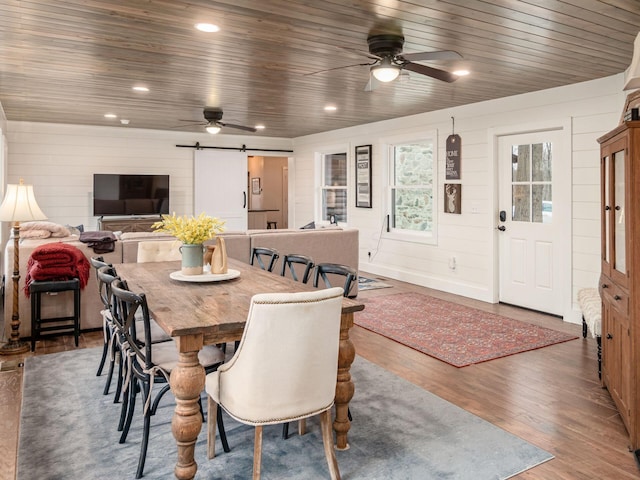 dining room featuring a barn door, wood walls, a ceiling fan, wood finished floors, and wood ceiling