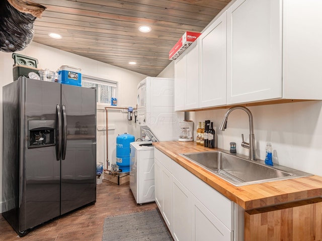kitchen with a sink, stainless steel fridge with ice dispenser, wooden counters, stacked washer / dryer, and wood finished floors