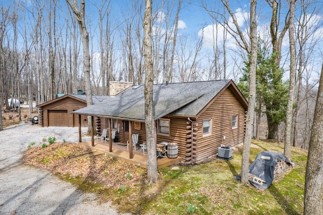 view of front of house featuring a detached garage, log siding, a porch, and roof with shingles