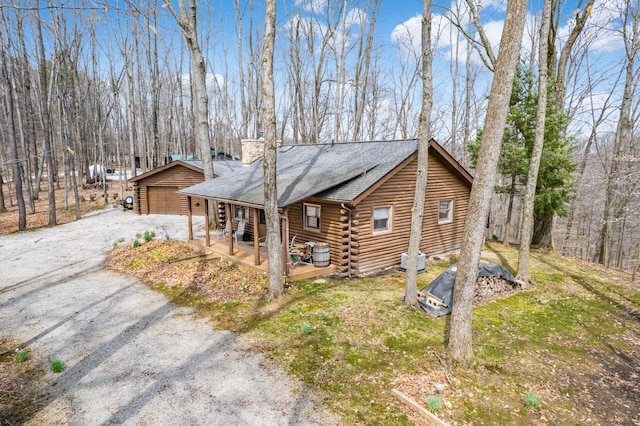 view of home's exterior featuring an outdoor structure, a chimney, a shingled roof, log siding, and a detached garage