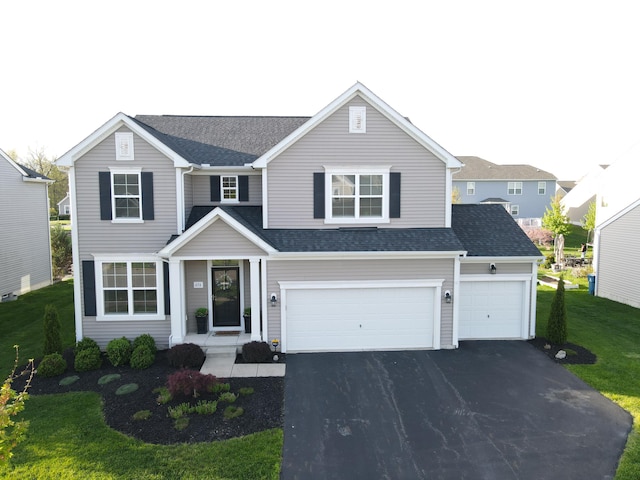 traditional-style home featuring driveway, roof with shingles, a front yard, and a garage
