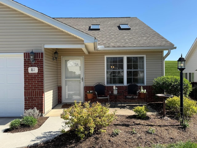 doorway to property featuring roof with shingles, an attached garage, a porch, and brick siding