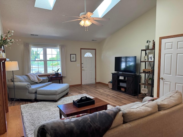living room with visible vents, baseboards, light wood-type flooring, vaulted ceiling with skylight, and a ceiling fan