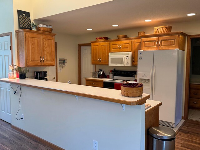 kitchen featuring dark wood finished floors, a peninsula, a kitchen bar, and white appliances