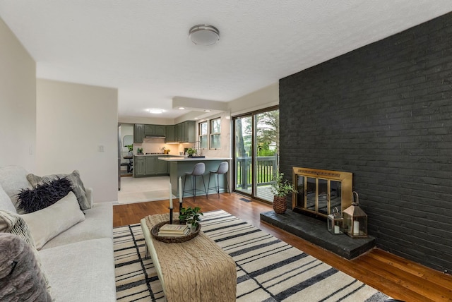 living area featuring a brick fireplace, brick wall, baseboards, and wood finished floors