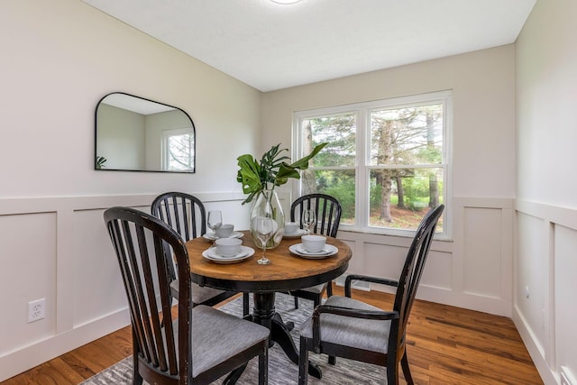 dining space with wood finished floors, a decorative wall, and a wainscoted wall
