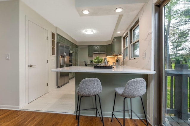 kitchen with light countertops, a peninsula, a breakfast bar, and stainless steel fridge with ice dispenser