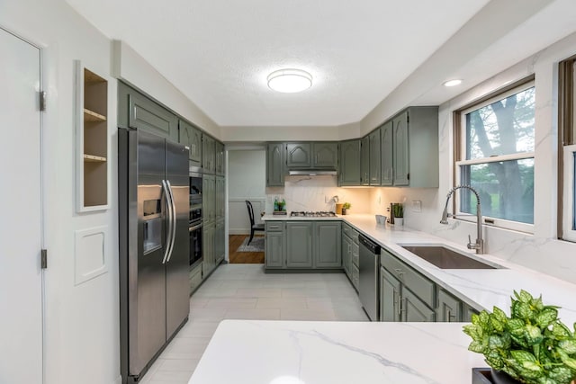 kitchen featuring green cabinetry, light stone counters, a sink, stainless steel appliances, and gray cabinetry