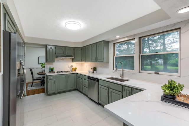 kitchen featuring stainless steel appliances, green cabinetry, light stone counters, and a sink