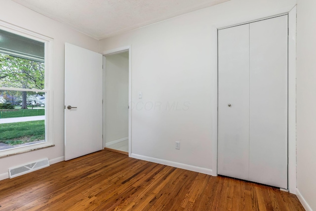 unfurnished bedroom with baseboards, a closet, wood finished floors, and visible vents
